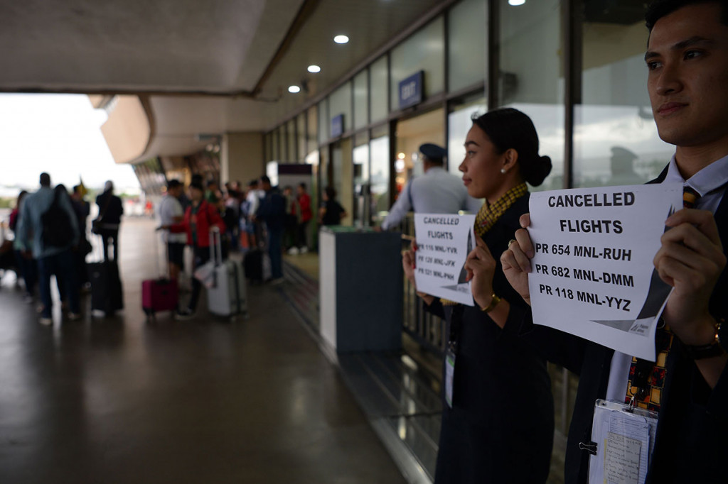 Staf maskapai penerbangan memegang plakat yang mengumumkan pembatalan penerbangan di terminal bandara internasional Manila, Selasa, 3 Desember 2019.