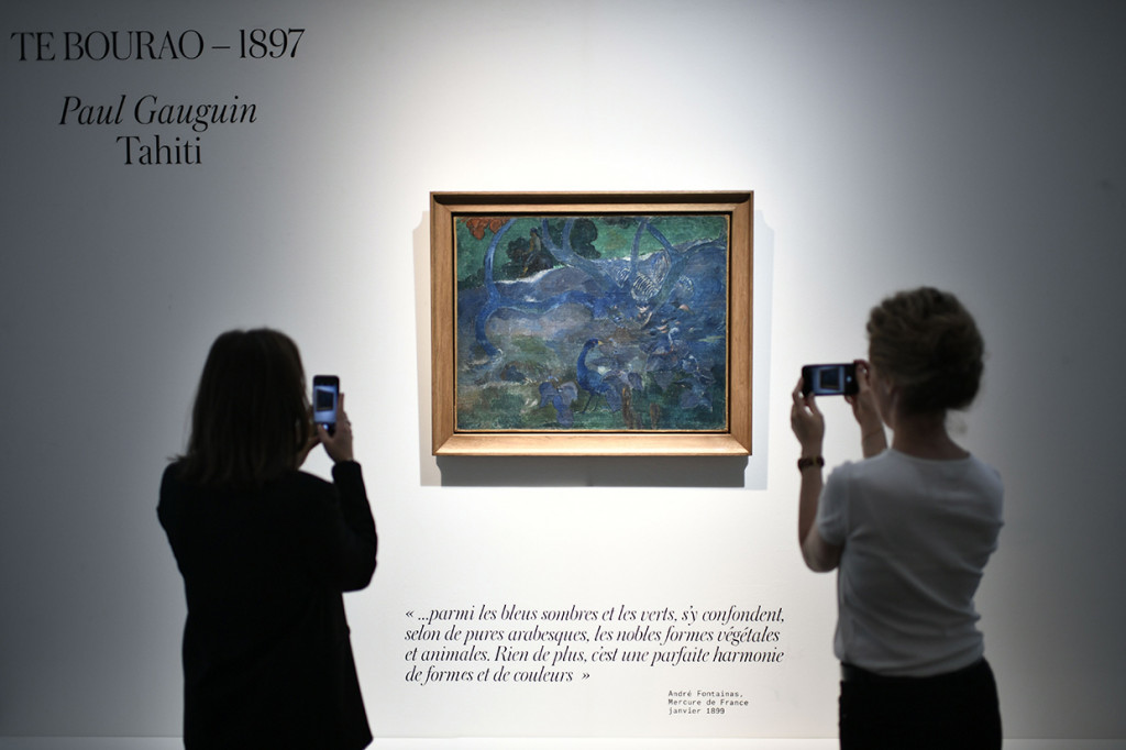 Dua wanita memotret lukisan karya seniman pasca-impresionis, Paul Gauguin, yang terjual Rp 148 miliar. 