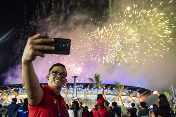 Seorang relawan melakukan swa foto dengan latar belakang kembang api saat penutupan SEA Games 2019 di Stadion Atletik New Clark City, Tarlac, Filipina.
