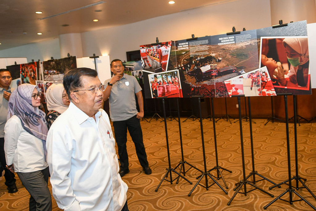 Mantan Wakil Presiden, yang juga Ketua Umum Palang Merah Indonesia (PMI) Jusuf Kalla (kedua kiri) menyaksikan jajaran foto kegiatan anggota PMI saat Musyawarah Nasional XXI PMI, di Jakarta.
