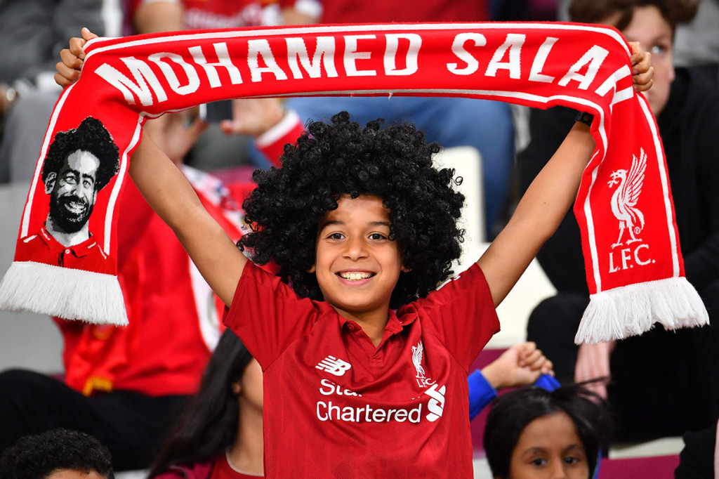 Fans cilik mengenakan wig kribo dan jersey Liverpool membentangkan syal bergambar Mohamed Salah dan foto pemain asal Mesir tersebut.