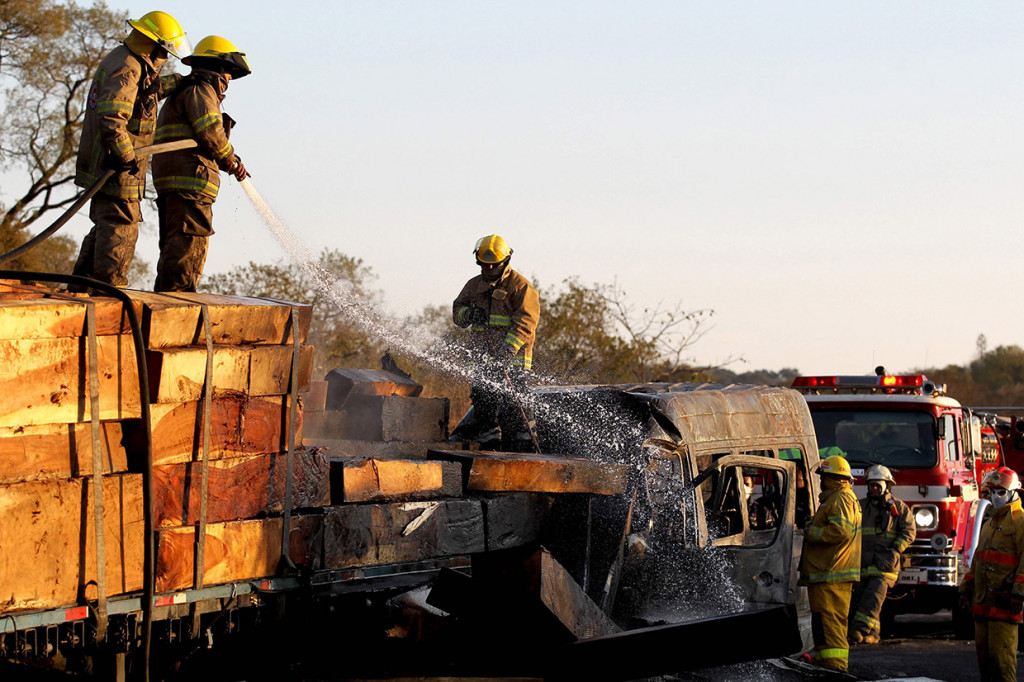 Petugas berusaha memadamkan api yang membakar mini bus dan truk yang bermuatan kayu pascaterjadinya kecelakaan di Meksiko, Rabu, 18 Desember 2019 waktu setempat.