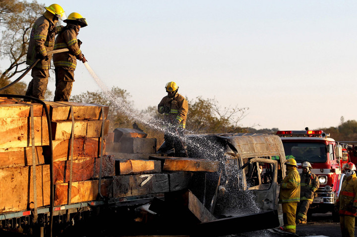 Petugas berusaha memadamkan api yang membakar mini bus dan truk yang bermuatan kayu pascaterjadinya kecelakaan di Meksiko, Rabu, 18 Desember 2019 waktu setempat.