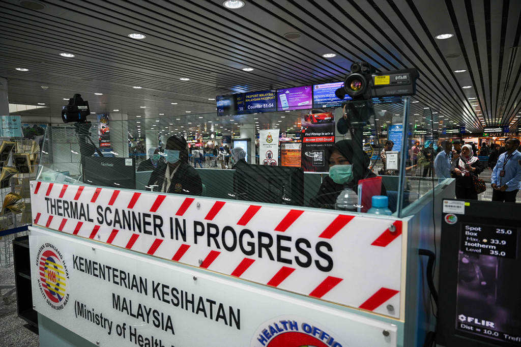 Petugas kesehatan memantau suhu tubuh penumpang yang tiba di Bandara Internasional Kuala Lumpur dengan thermal scanner.
