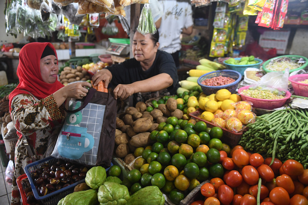 Pedagang memasukkan belanjaan ke dalam tas belanjaan saat bertransaksi di Pasar Tebet Barat, Jakarta.