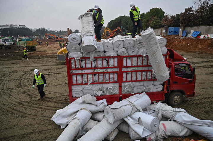 Para pekerja menurunkan bahan-bahan dari sebuah truk di lokasi pembangunan rumah sakit baru yang sedang dibangun untuk merawat pasien dari wabah virus mematikan di Wuhan, Provinsi Hubei.