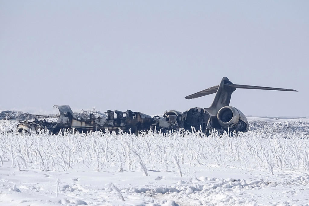 Badan pesawat berada di sebuah lapangan yang ditutupi salju. Asap terus mengepul dari puing pesawat tersebut.