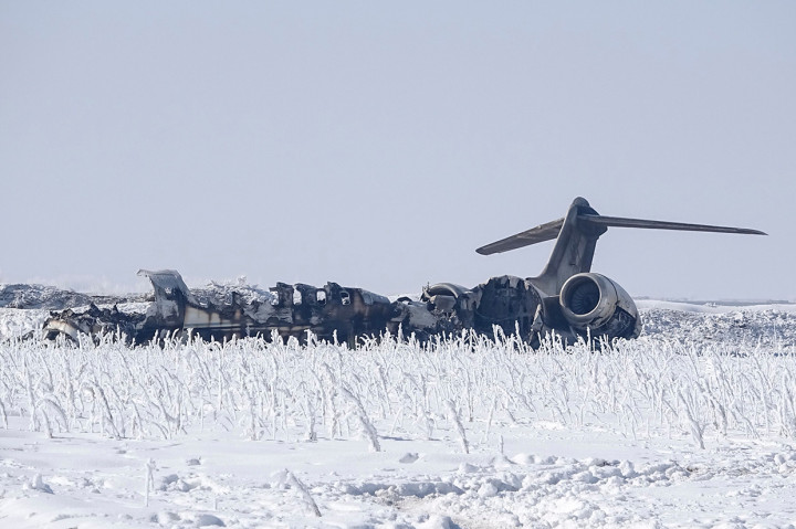 Badan pesawat berada di sebuah lapangan yang ditutupi salju. Asap terus mengepul dari puing pesawat tersebut.