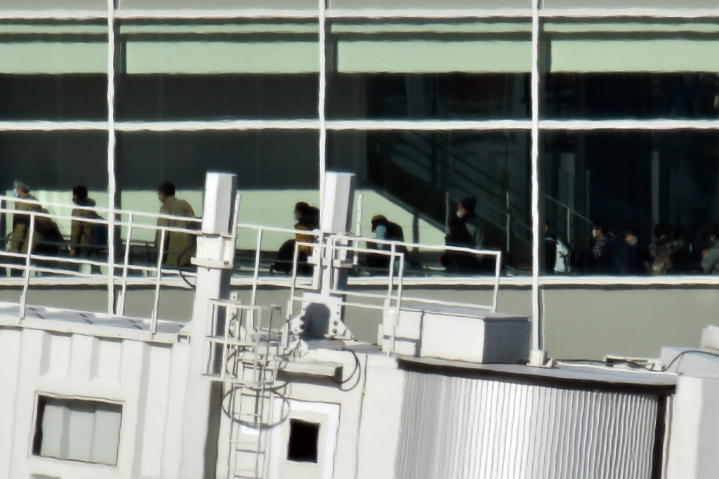 Para penumpang yang tiba dari Wuhan terlihat berjalan memasuki terminal di Bandara Internasional Haneda, Tokyo.