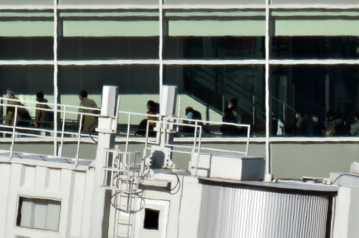 Para penumpang yang tiba dari Wuhan terlihat berjalan memasuki terminal di Bandara Internasional Haneda, Tokyo.
