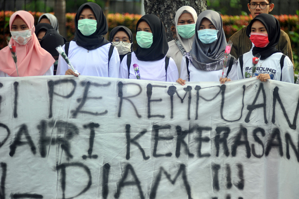 Sejumlah mahasiswi memegang bunga mawar dan menggunakan masker sambil memperlihatkan spanduk kampanye Anti Kekerasan Seksual Terhadap Perempuan, di Padang, Sumatera Barat. 