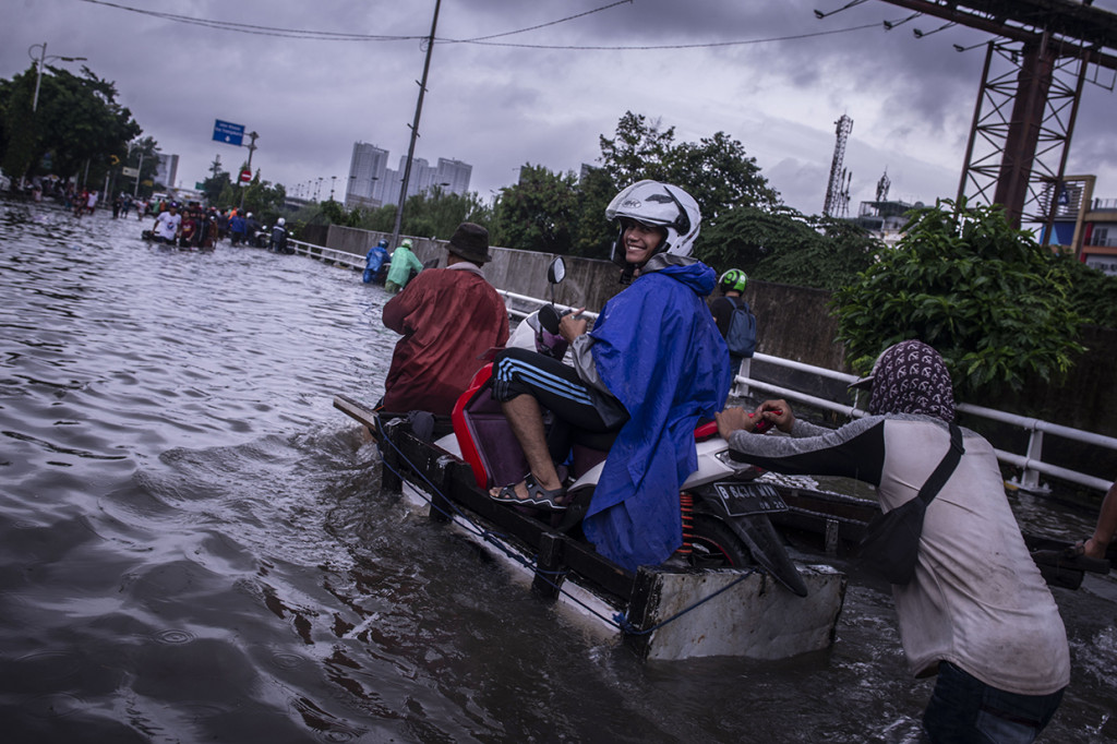 Pengendara sepeda motor menggunakan jasa angkut gerobak saat melintasi banjir di kawasan Grogol, Jakarta. ANTARA FOTO/Aprillio Akbar