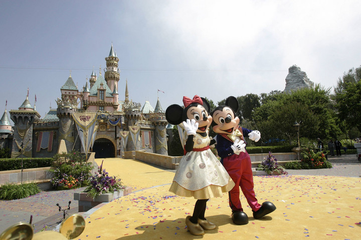 Karakter Disney, Mickey Mouse dan Minnie Mouse melambaikan tangan ke kerumunan orang di depan Sleeping Beauty Castle selama peringatan ke-50 tahun pembukaan Disneyland di Anaheim, California, pada 17 Juli 2005 silam. Walt Disney Co akan menutup taman hiburan di California dan Florida, serta resor di Paris mulai akhir pekan ini hingga akhir bulan, karena wabah global virus korona jenis baru covid-19.