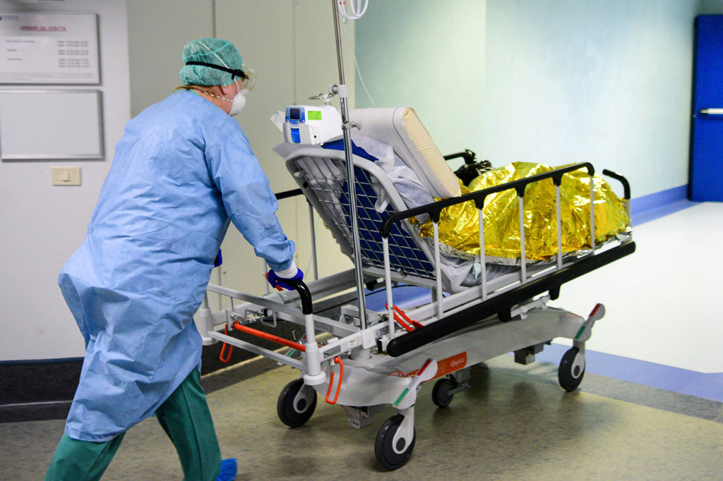 Seorang petugas medis yang mengenakan menutup muka dan peralatan perlindungan membawa seorang pasien ke dalam unit perawatan intensif virus korona di Rumah Sakit Brescia Poliambulanza, Lombardy, pada 17 Maret 2020 waktu setempat. 