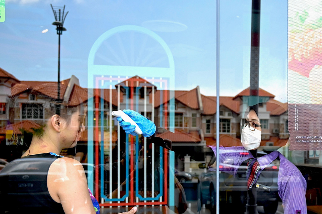 Pekerja restoran cepat saji mengukur suhu tubuh pengunjung yang datang saat hari pertama kebijakan lockdown di Malaysia.