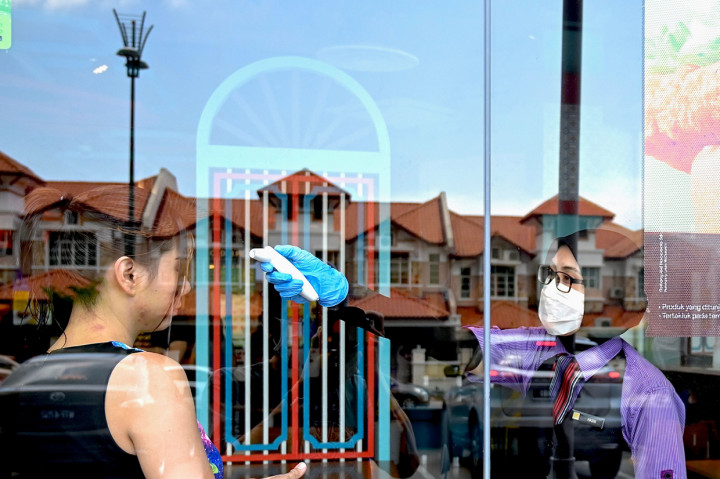 Pekerja restoran cepat saji mengukur suhu tubuh pengunjung yang datang saat hari pertama kebijakan lockdown di Malaysia.