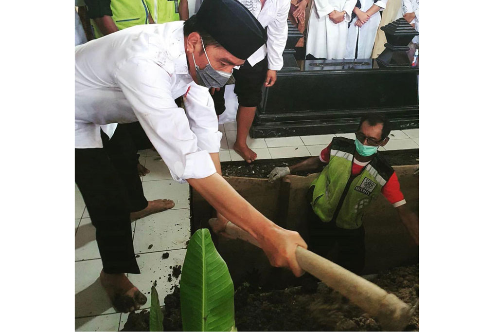 Foto lainnya menunjukkan Presiden memasukkan tanah ke liang lahat menggunakan cangkul. Tanah mengotori kemejanya.