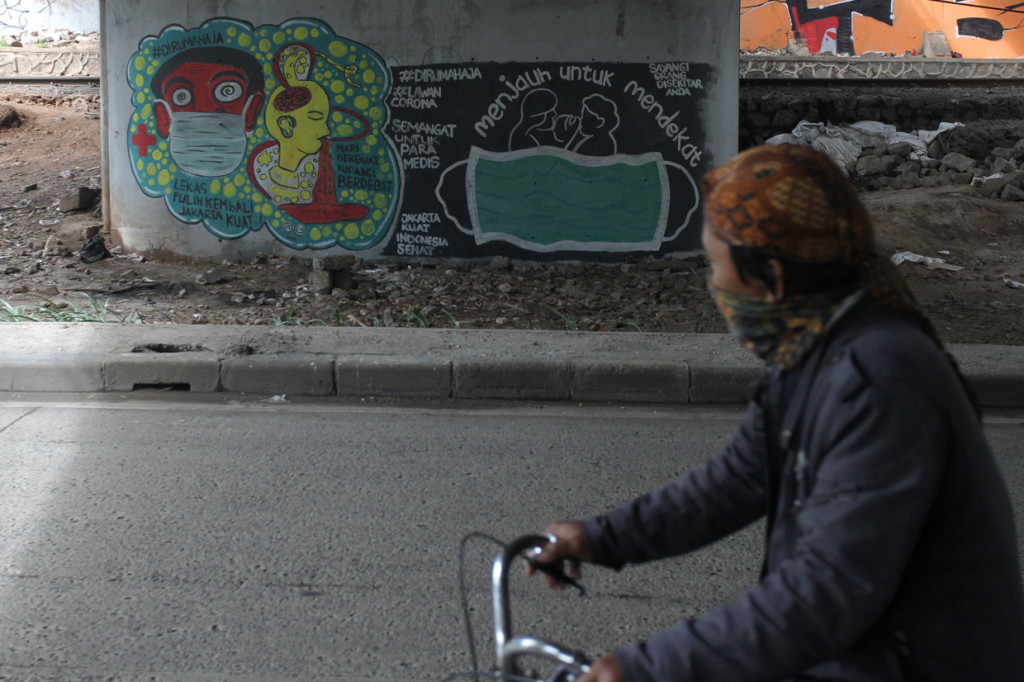 Warga melintasi mural ajakan untuk menggunakan masker dan tetap di rumah di kolong Jalan Rasuna Said, Jakarta.