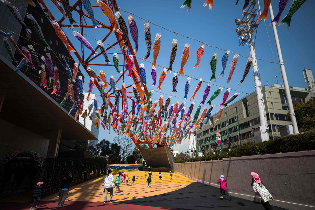 Anak-anak TK bermain di bawah windsocks berbentuk ikan mas atau 'koinobori' di sebelah Menara Tokyo pada 8 April 2020.