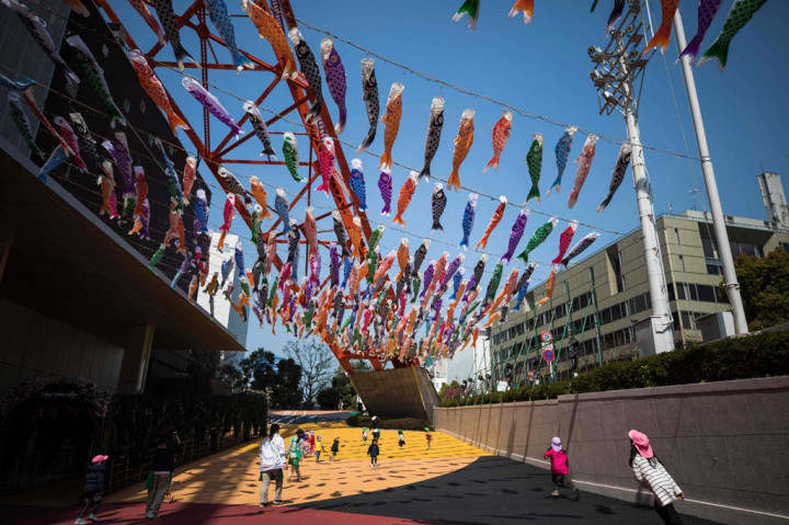 Anak-anak TK bermain di bawah windsocks berbentuk ikan mas atau 'koinobori' di sebelah Menara Tokyo pada 8 April 2020.