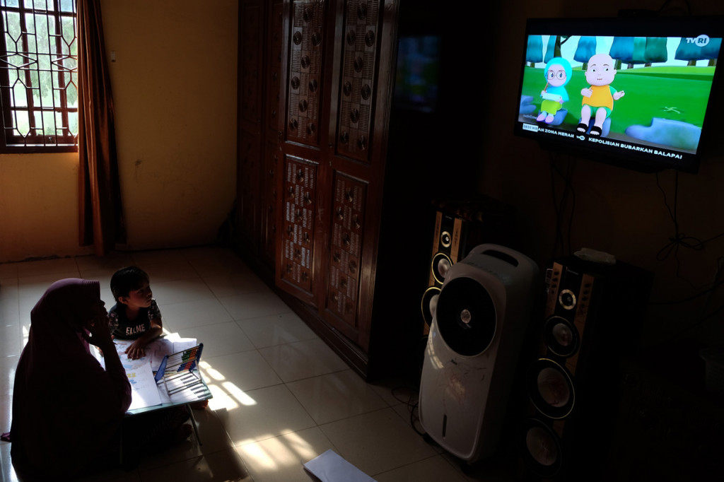 Seorang anak didampingi ibunya belajar dengan melihat tayangan siaran TVRI di rumah mereka, di Deli Serdang, Sumatera Utara.