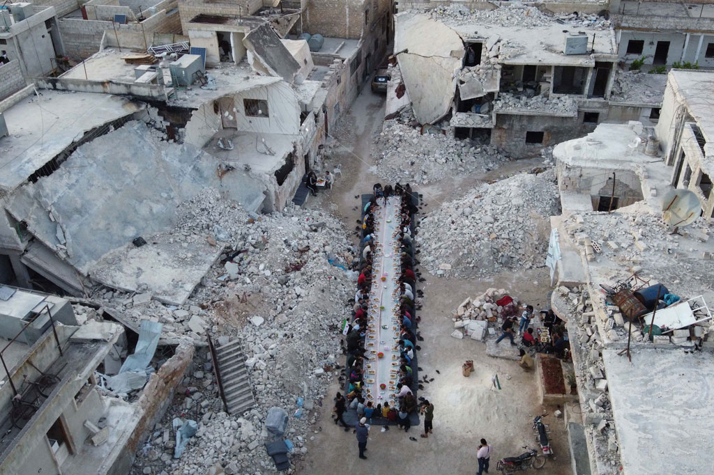 Warga Suriah berada di antara reruntuhan bangunan di lingkungan mereka yang hancur saat acara berbuka puasa  yang diselenggarakan oleh badan amal setempat di Kota Atareb, Aleppo, Suriah, Kamis, 7 Mei 2020.