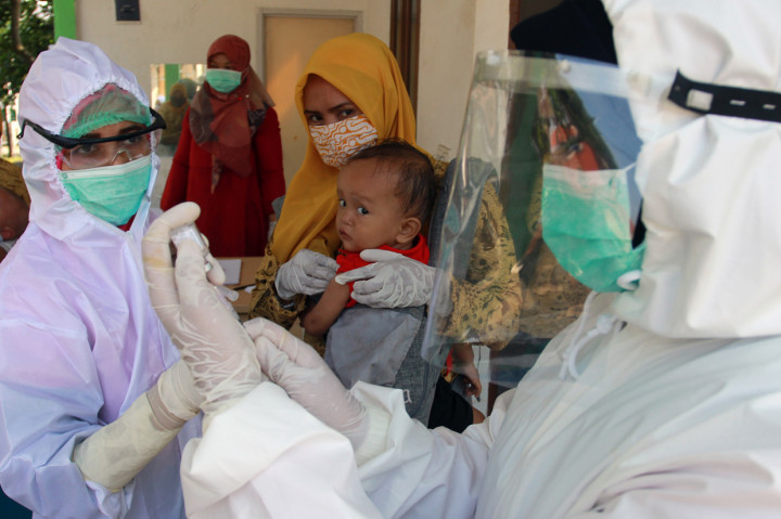 Petugas medis dengan menggunakan alat pelindung diri (APD) dari Puskesmas Babakan memberikan imunisasi kepada seorang balita di Posbindu Cempaka 2 Babakan, Tangerang Selatan, Banten.