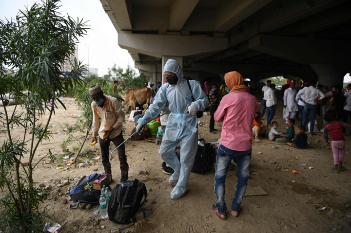 Petugas menyemprotkan disinfektan di tempat para pekerja migran menunggu transportasi untuk kembali ke kota asal mereka di Uttar Pradesh dan negara-negara Bihar. AFP Photo/Sajjad Hussain