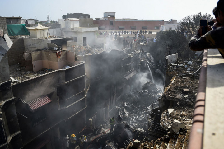 Petugas penyelamat berusaha mengevakuasi korban, sementara petugas pemadam berusaha memadamkan api di lokasi kecelakaan pesawat di kawasan permukiman di Karachi, Pakistan, Jumat, 22 Mei 2020.