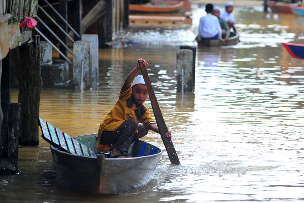 Anak-anak menggunakan perahu melintasi jalan permukiman yang terendam banjir luapan Sungai Batanghari saat perayaan Idul Fitri 1441 Hijriah di Tahtul Yaman, Pelayangan, Jambi, Minggu, 24 Mei 2020.