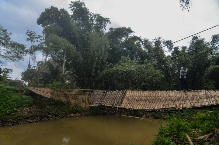 Warga bergelantungan saat melintasi jembatan rusak di Desa Banjarsari, Kabupaten Tasikmalaya.