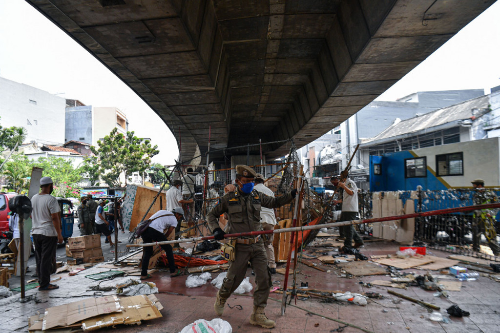 Anggota Satpol PP membersihkan lapak pedagang yang berjualan di kolong jembatan layang Pasar Pagi Asemka, Jakarta Barat.