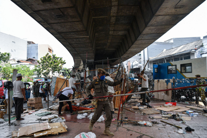 Anggota Satpol PP membersihkan lapak pedagang yang berjualan di kolong jembatan layang Pasar Pagi Asemka, Jakarta Barat.