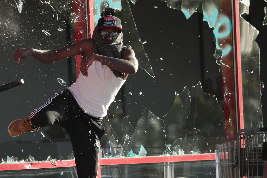 Seorang demonstran memecahkan jendela kaca sebuah pertokoan saat protes menuntut keadilan atas kematian warga kulit hitam George Floyd di St Paul, Minnesota, Kamis, 28 Mei 2020 waktu setempat.