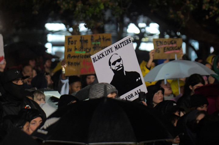 Para pengunjuk rasa di Kota Auckland, Selandia Baru, duduk di jalan setelah pawai damai dan mereka mengangkat kepalan tangan sebagai suatu tanda untuk persatuan, solidaritas, dan Kekuatan Warga Kulit Hitam.