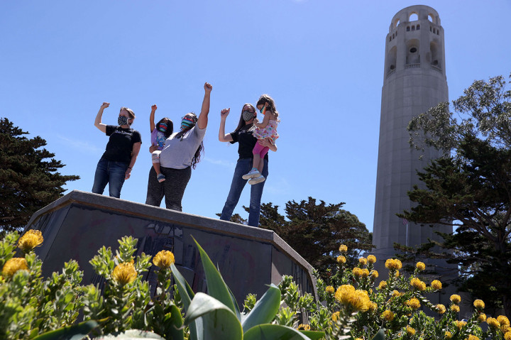 Warga berdiri dengan mengepalkan tangan di atas alas beton di mana sebuah patung Christopher Columbus pernah berdiri di kaki Coit Tower di San Francisco, California, Kamis, 18 Juni 2020 waktu setempat.