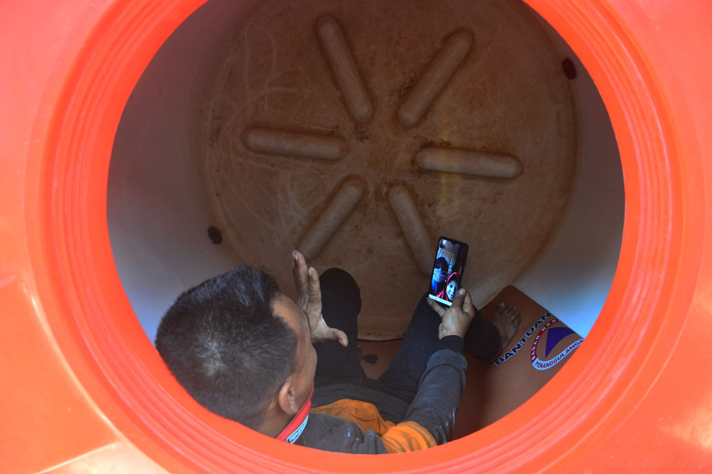 Relawan covid-19 Badan Penanggulangan Bencana Daerah (BPBD) Kabupaten Kudus, Kristanto, melakukan panggilan video kepada istri dan anak di dalam tangki air yang menjadi tempat tinggalnya di markas BPBD Kudus, Jawa Tengah, Jumat, 3 Juli 2020.