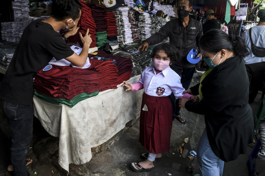 Calon pembeli mengenakan pakaian seragam sekolah kepada anaknya di Pasar Jatinegara, Jakarta.