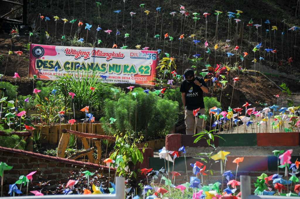 Warga melintas di antara hiasan kincir kertas warna-warni di Desa Wisata Lahan Hutan Raya Mulung Layung di Babakan Cipanas, Kabupaten Sumedang, Jawa Barat, Sabtu, 25 Juli 2020.