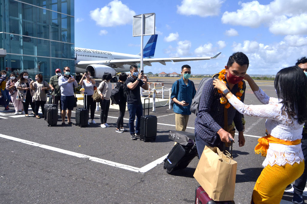 Petugas mengalungkan bunga saat menyambut penumpang pesawat rute domestik yang tiba di Bandara Internasional I Gusti Ngurah Rai, Badung, Bali, Jumat, 31 Juli 2020.