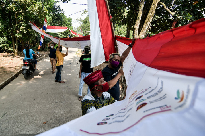Warga memasang umbul-umbul merah putih dari tas bantuan Presiden di Jalan Caringin, Bedahan, Depok, Jawa Barat.