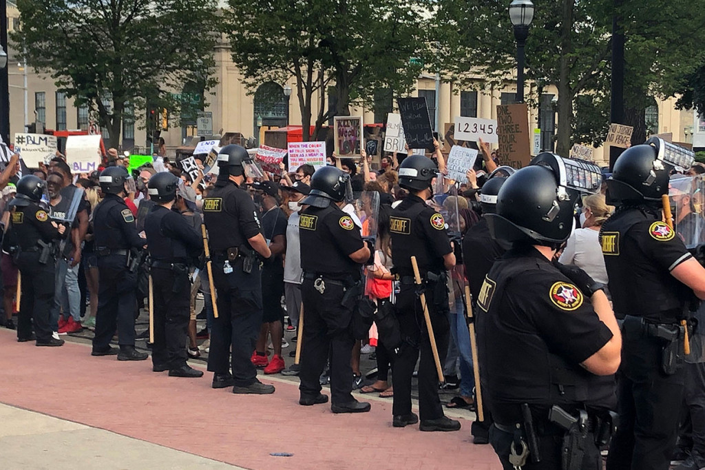 Sekitar dua lusin petugas Sheriff Kenosha County berdiri di depan gedung pengadilan ketika para pengunjuk rasa di seberang jalan menyerukan keadilan rasial. Sementara helikopter berputar-putar di atas kepala serta petugas terlihat ditempatkan di atap gedung pengadilan.