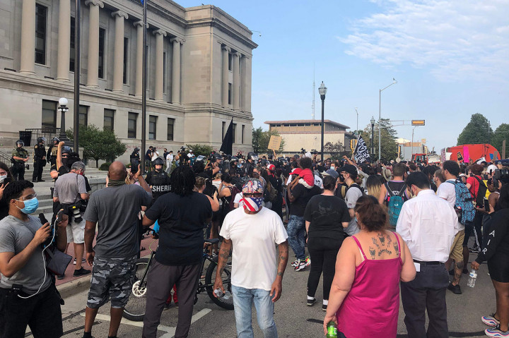 Sekitar dua lusin petugas Sheriff Kenosha County berdiri di depan gedung pengadilan ketika para pengunjuk rasa di seberang jalan menyerukan keadilan rasial. Sementara helikopter berputar-putar di atas kepala serta petugas terlihat ditempatkan di atap gedung pengadilan.