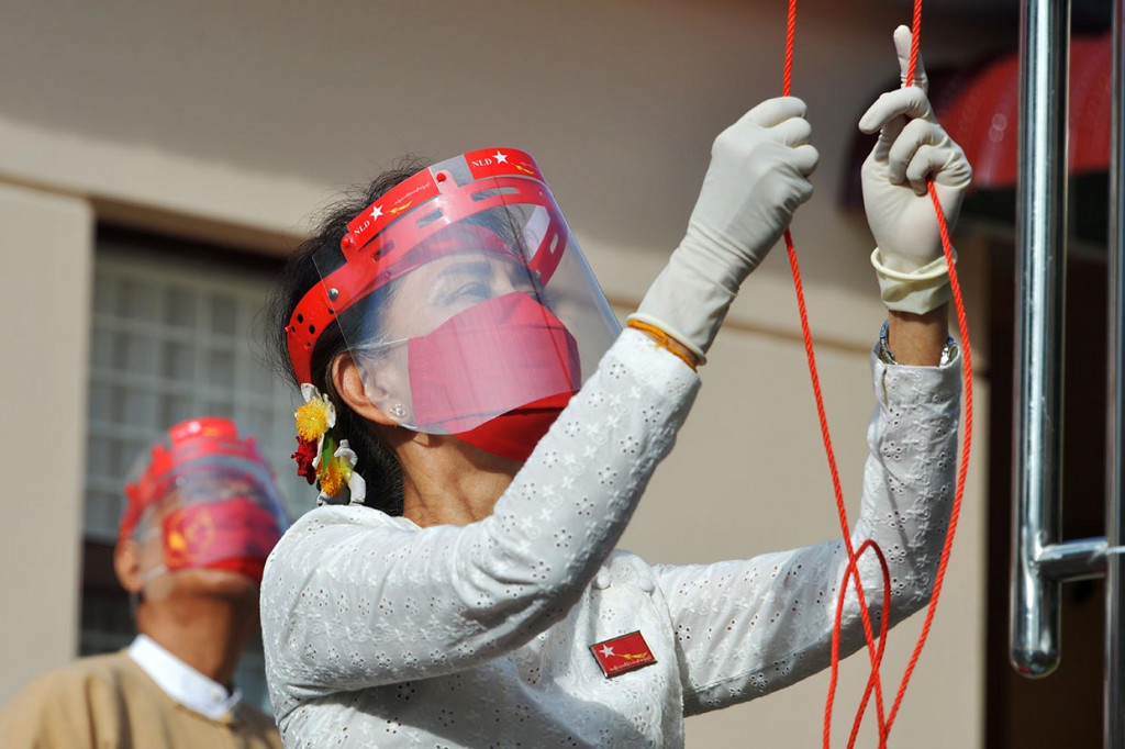 Mengenakan masker wajah berwarna merah, face shield, dan sarung tangan karet, Suu Kyi Selasa pagi mengibarkan bendera National League for Democracy (NLD) - dengan simbol merak tarung - di dalam sebuah upacara kecil kantor partai di ibu kota, Naypyidaw.