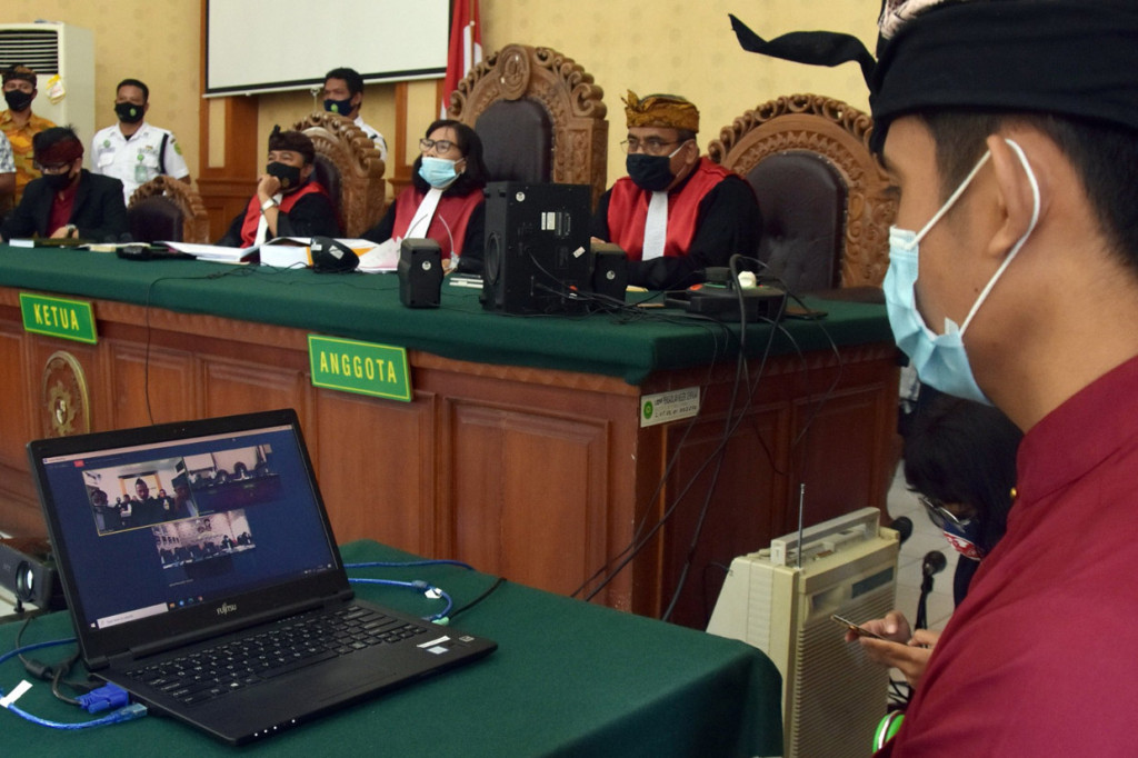 Petugas memantau jalannya sidang perdana drummer grup musik Superman is Dead (SID) I Gede Ari Astina alias Jerinx dalam kasus ujaran kebencian dan pencemaran nama baik yang digelar secara daring di Pengadilan Negeri Denpasar, Bali.