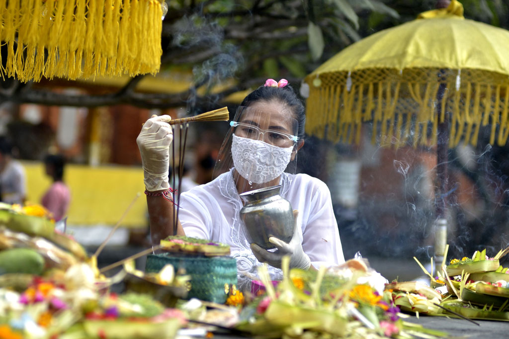 Pemuka agama Hindu dengan mengenakan face sield memercikkan air suci saat persembahyangan Hari Raya Galungan di Pura Jagatnatha, Denpasar, Bali, Rabu, 16 September 2020.