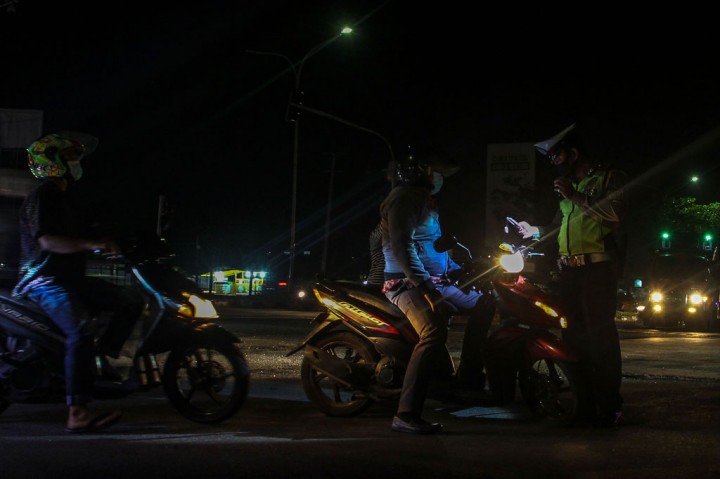 Petugas Satlantas Polresta Pekanbaru memeriksa identitas kependudukan warga yang hendak melintas ketika penerepan jam malam pembatasan sosial berskala mikro (PSBM) di Kecamatan Tampan, Pekanbaru, Riau, Rabu, 16 September 2020 malam.