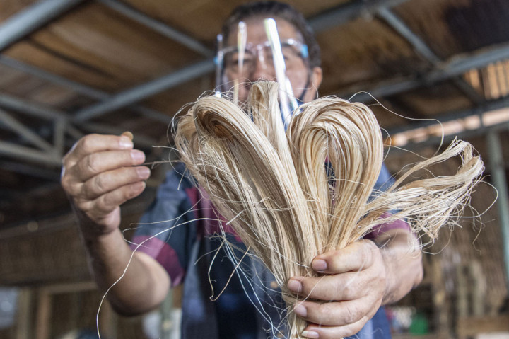 Jarum jam di dinding hampir menunjukkan pukul 12.00. Puluhan pekerja masih terlarut dalam kesibukannya menganyam pintalan serat pohon pisang (Abaca fiber) di alat tenun bukan mesin (ATBM) di bengkel anyam milik Djunaedi yang terletak di Jalan Sukarela, Kota Palembang, Sumatera Selatan.