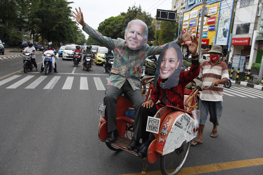 Warga menggunakan topeng berwajah pasangan Presiden Amerika Serikat terpilih Joe Biden (kiri) dan Wakil Presiden Kamala Harris (kanan) di Jalan Slamet Riyadi, Solo, Jawa Tengah.