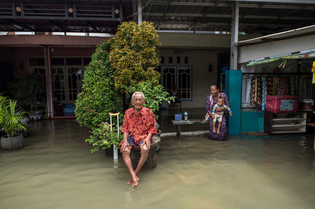 Warga duduk di luar rumah mereka yang terendam banjir di Gresik, Jawa Timur.